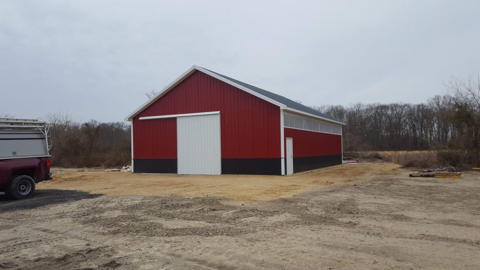 Red barn with white doors on a gravel lot under a cloudy sky