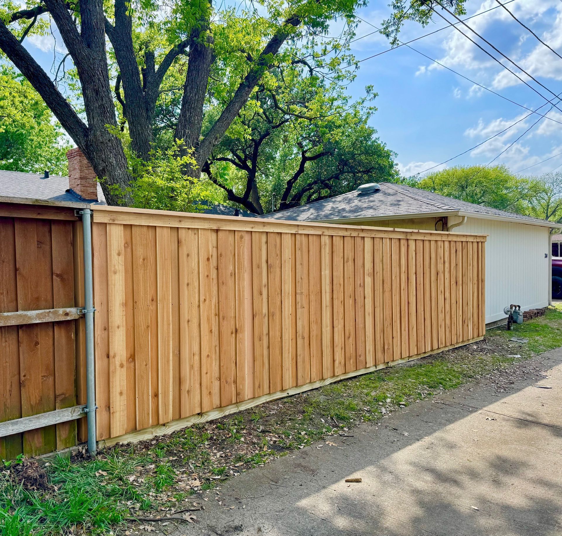A wooden fence is along the side of a dirt road next to a house.