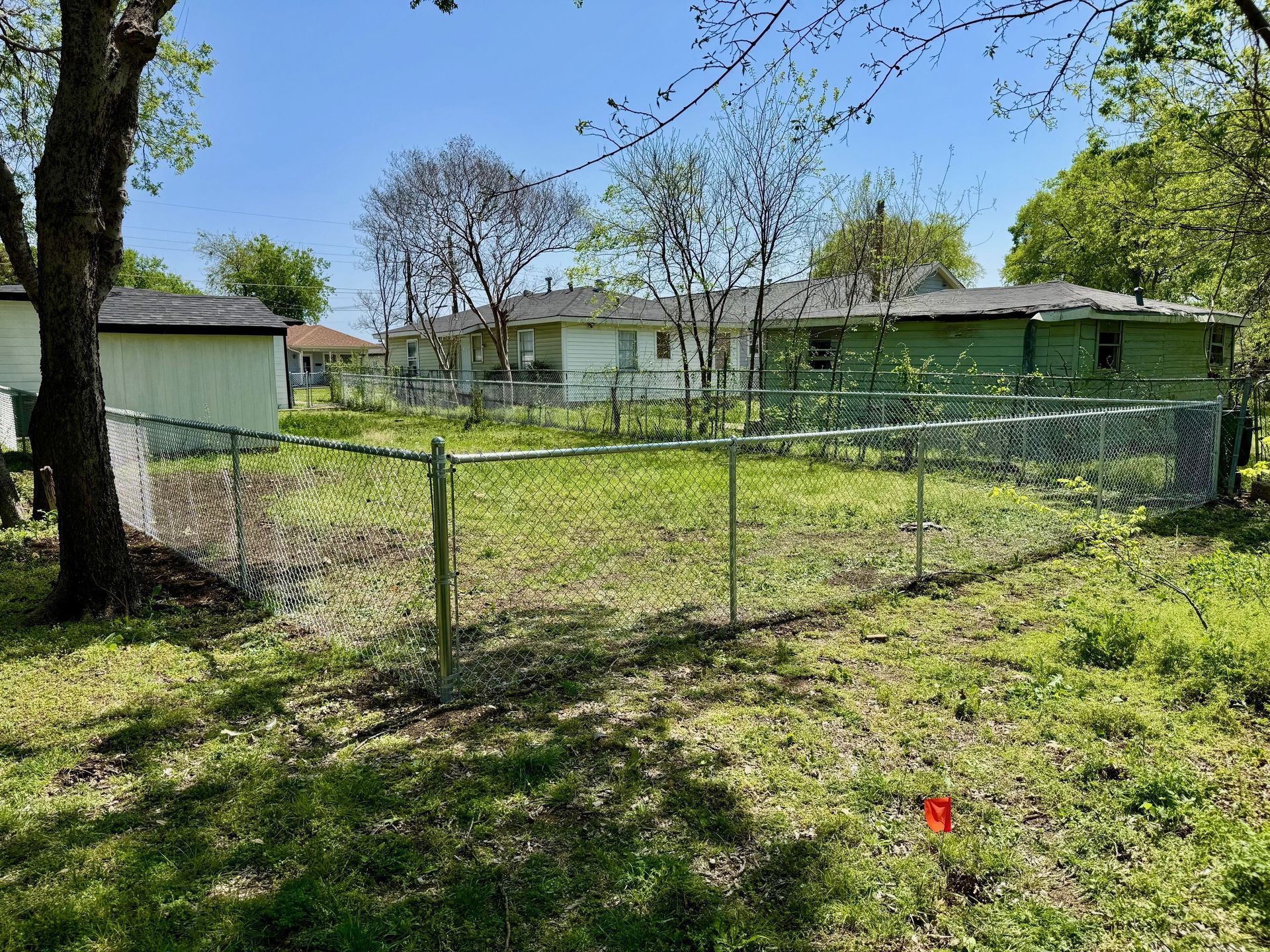 A chain link fence surrounds a grassy yard in front of a house.