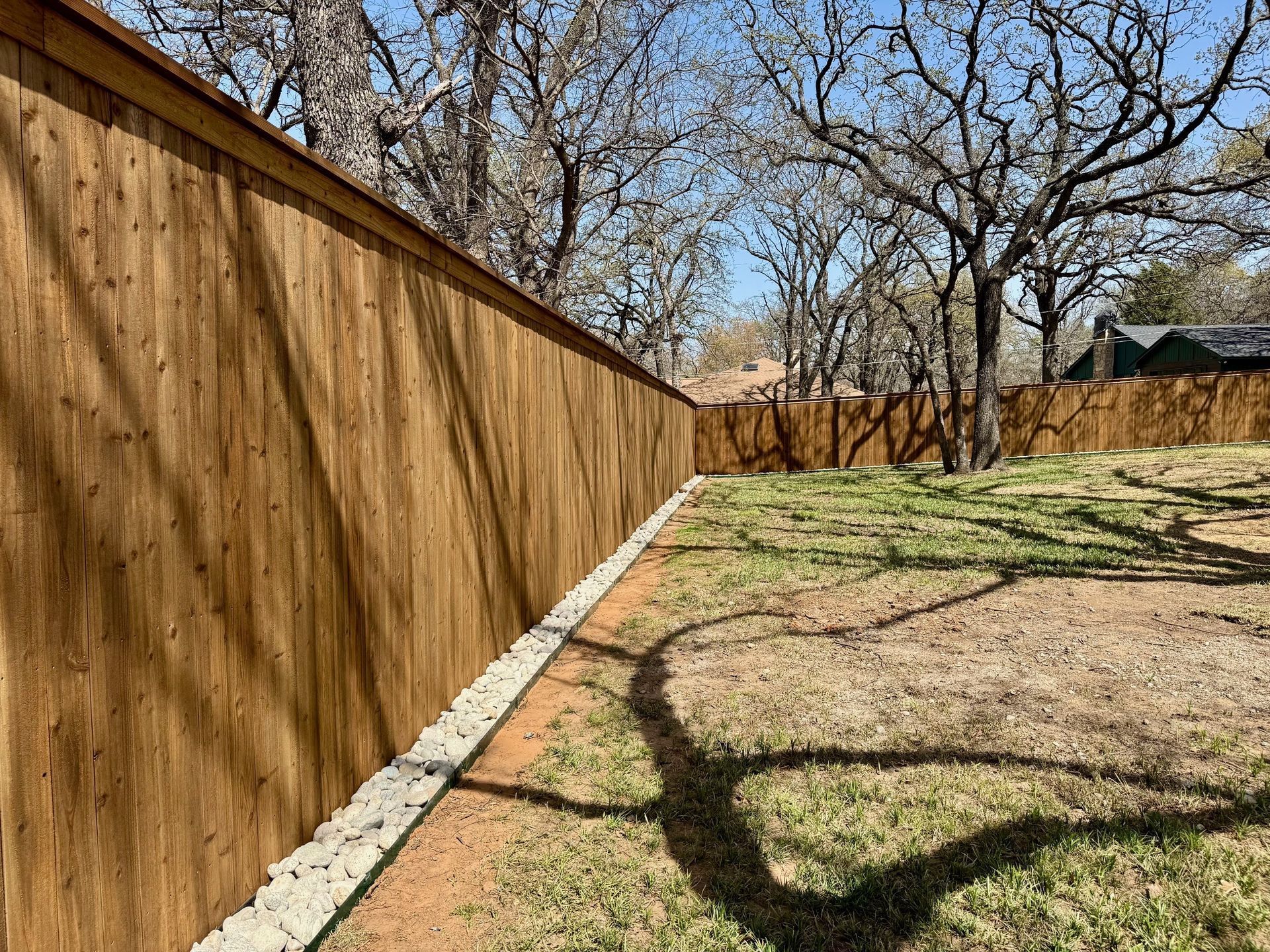 A wooden fence surrounds a grassy yard with trees in the background.