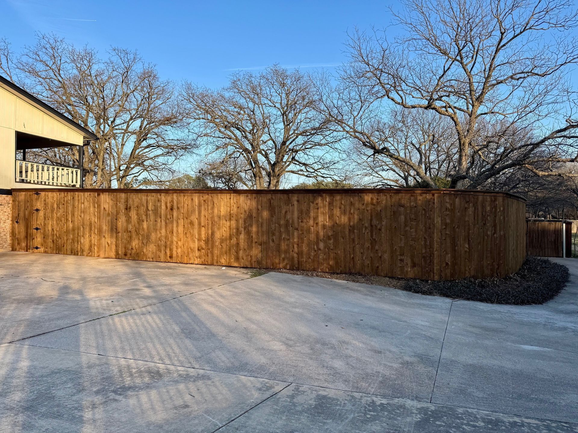 A wooden fence is surrounding a driveway in front of a house.