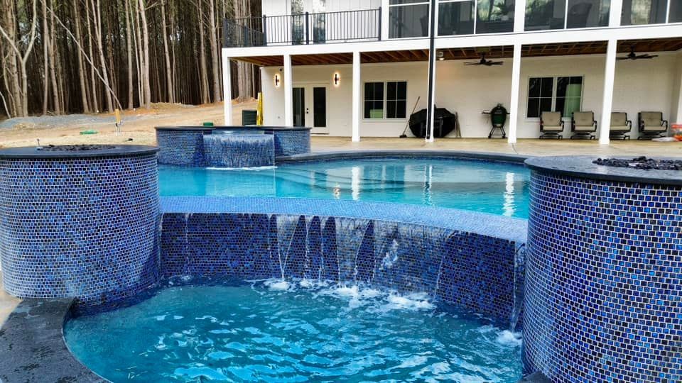 A large swimming pool with a waterfall in front of a house.