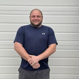 Man in navy shirt stands in front of a white garage door, arms crossed, smiling.