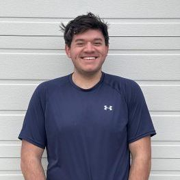 Man in a navy blue t-shirt smiles in front of a white horizontal-paneled wall.