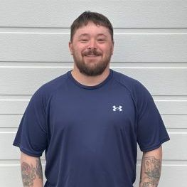 Man with a beard in a blue Under Armour shirt smiles in front of a white wall.