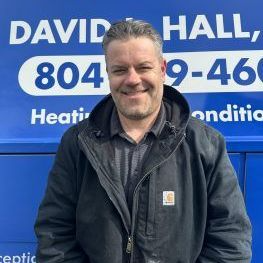 Man in a black jacket smiles in front of a blue van with
