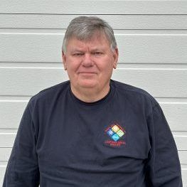 Man wearing a dark blue long-sleeve shirt stands in front of a white horizontal wall.