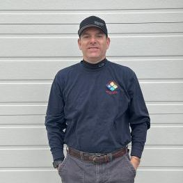Man in black hat and long-sleeve shirt stands in front of a white garage door.