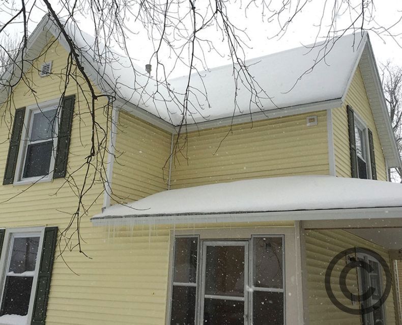 A yellow house with black shutters and snow on the roof