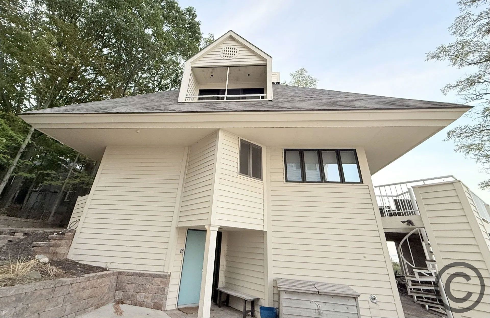 Beige building with a dormer and staircase. Trees surround the structure, exterior view.