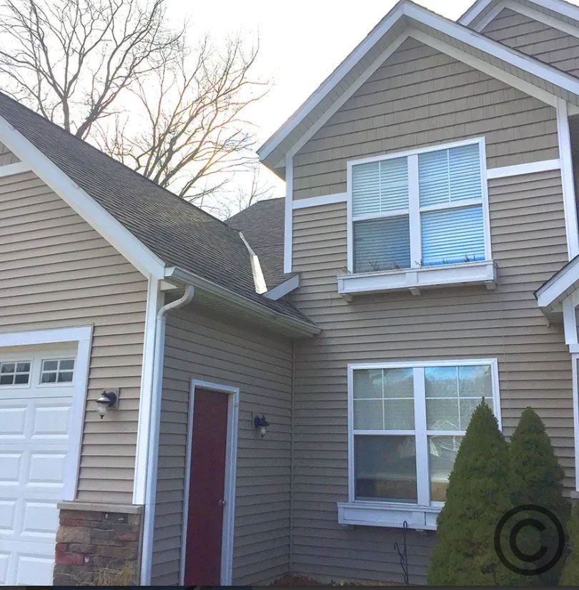 Beige house with white trim, red door, and two-car garage. Two windows are visible.