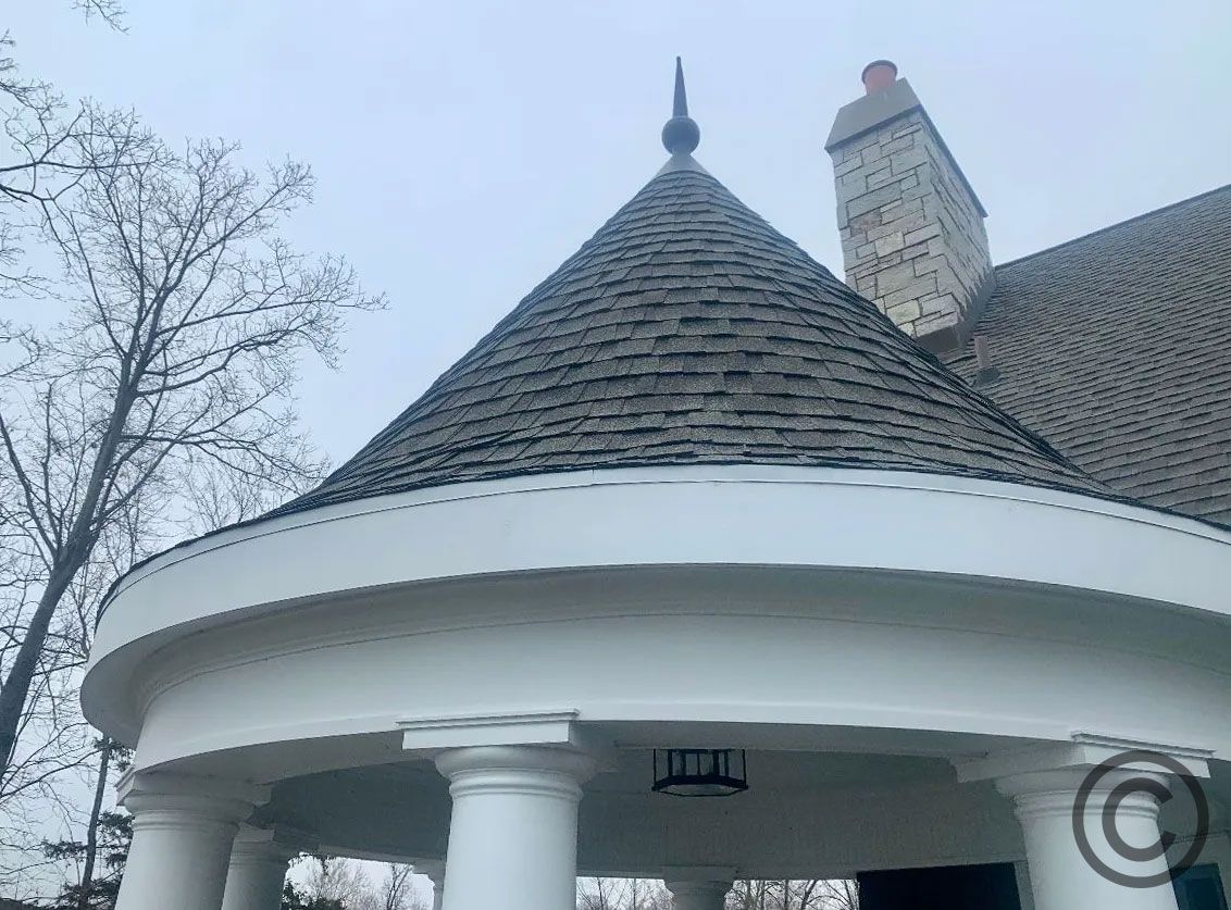 White curved porch with a conical roof and chimney against a cloudy sky.