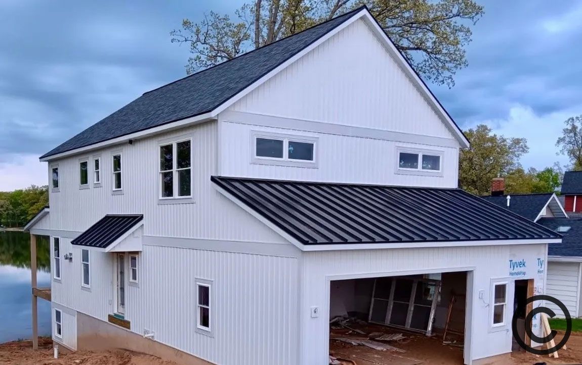 White two-story house with dark roof and attached garage near water, under cloudy sky.