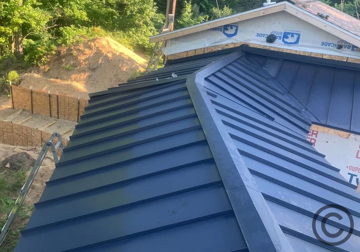 Blue metal roof being installed on a house with a curved section; outdoor setting.