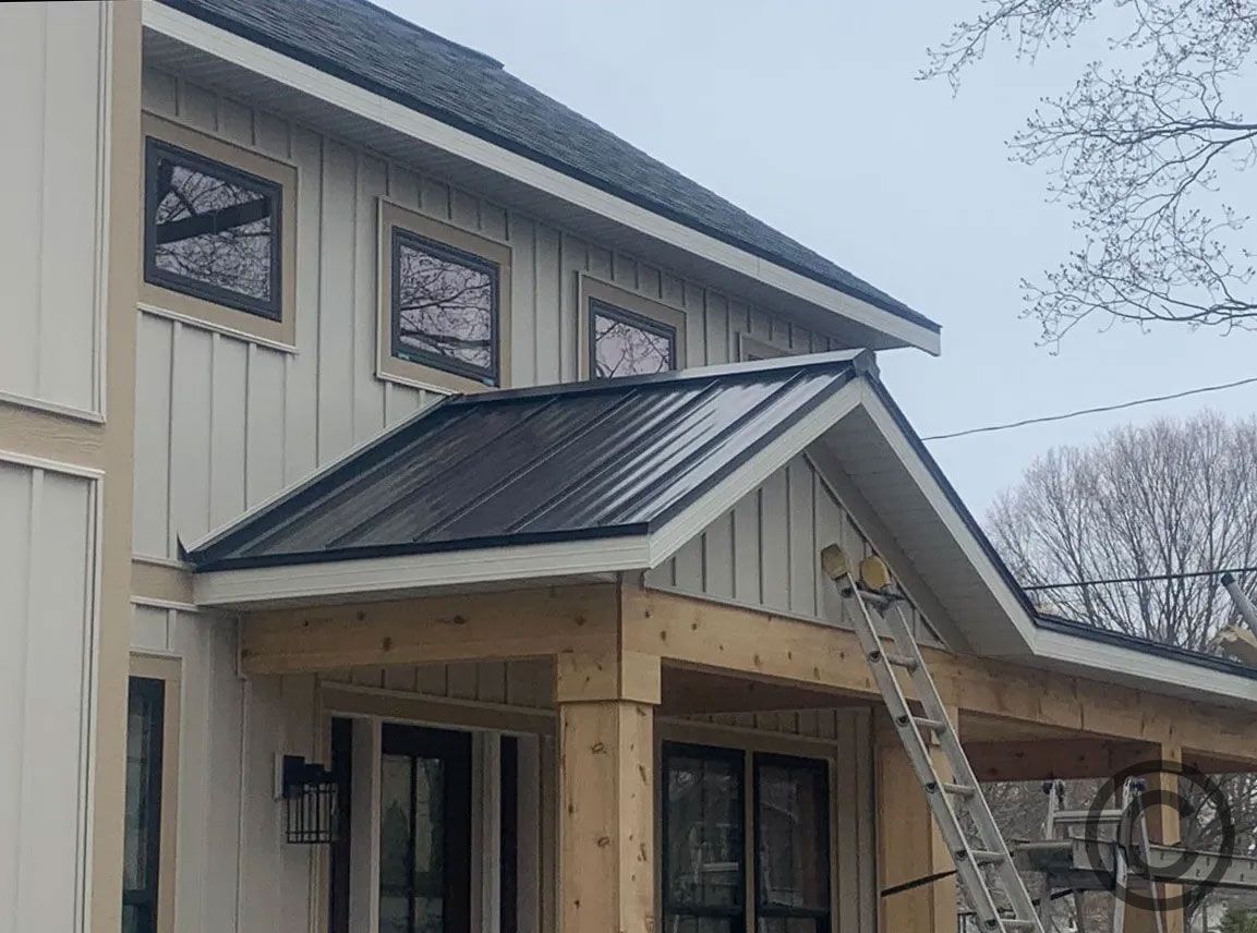 Exterior of a light-colored house with a black metal roof and wooden porch under construction.