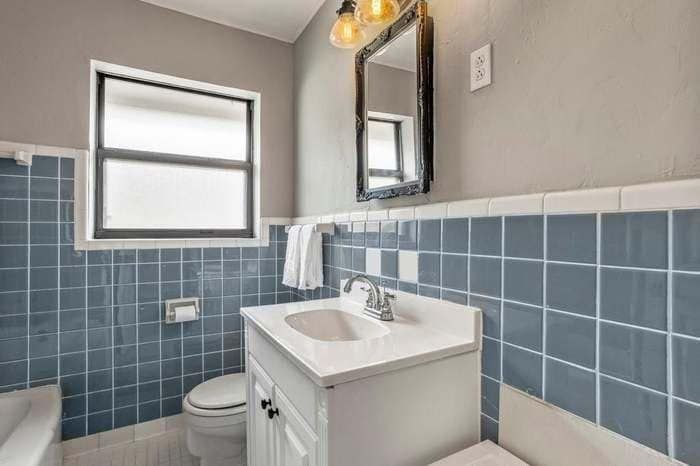 A bathroom with blue tiles , a sink , toilet , and mirror.