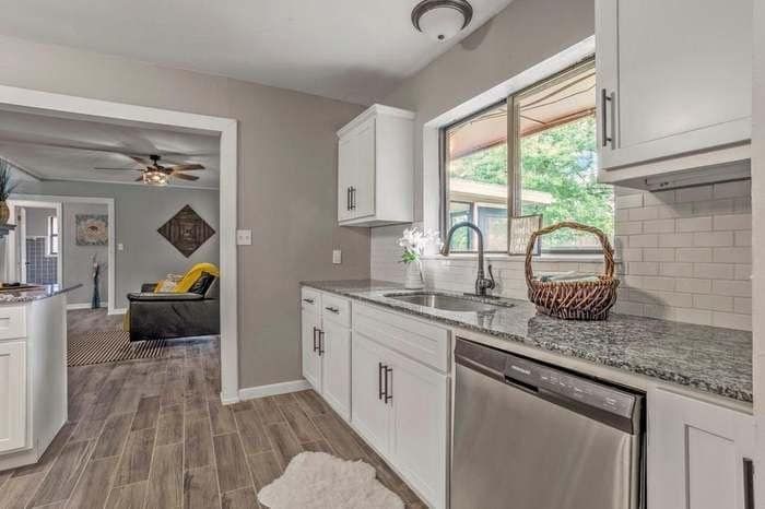 A kitchen with white cabinets , granite counter tops , a sink and a dishwasher.