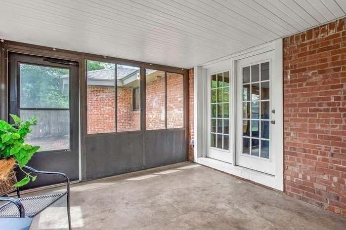 A screened in porch with a brick wall and white doors.