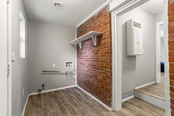 A laundry room with a brick wall and a wooden floor.