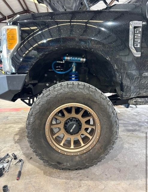 A black truck with gold wheels and tires is parked in a garage.