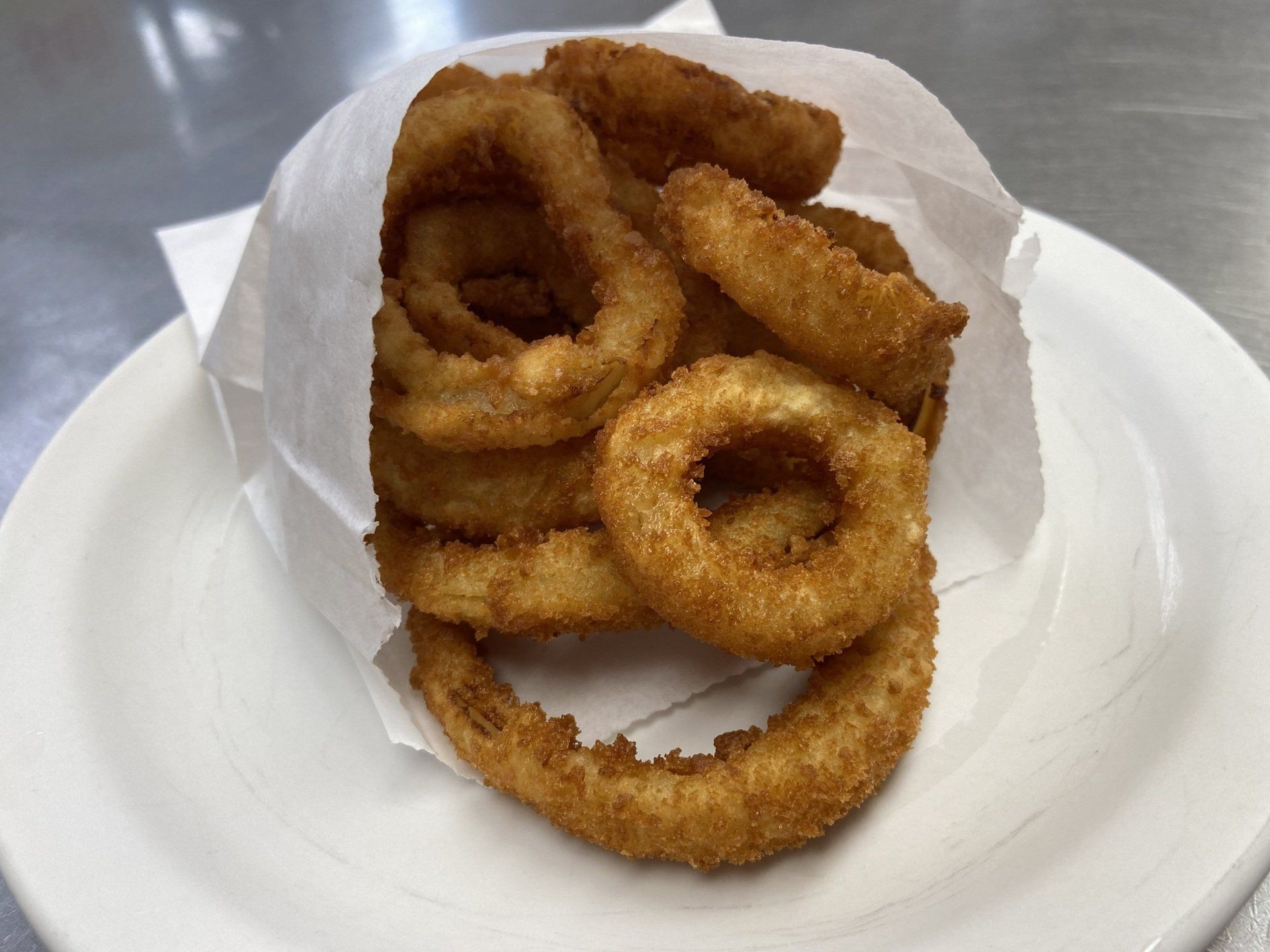A paper bag of golden-brown onion rings on a white plate.