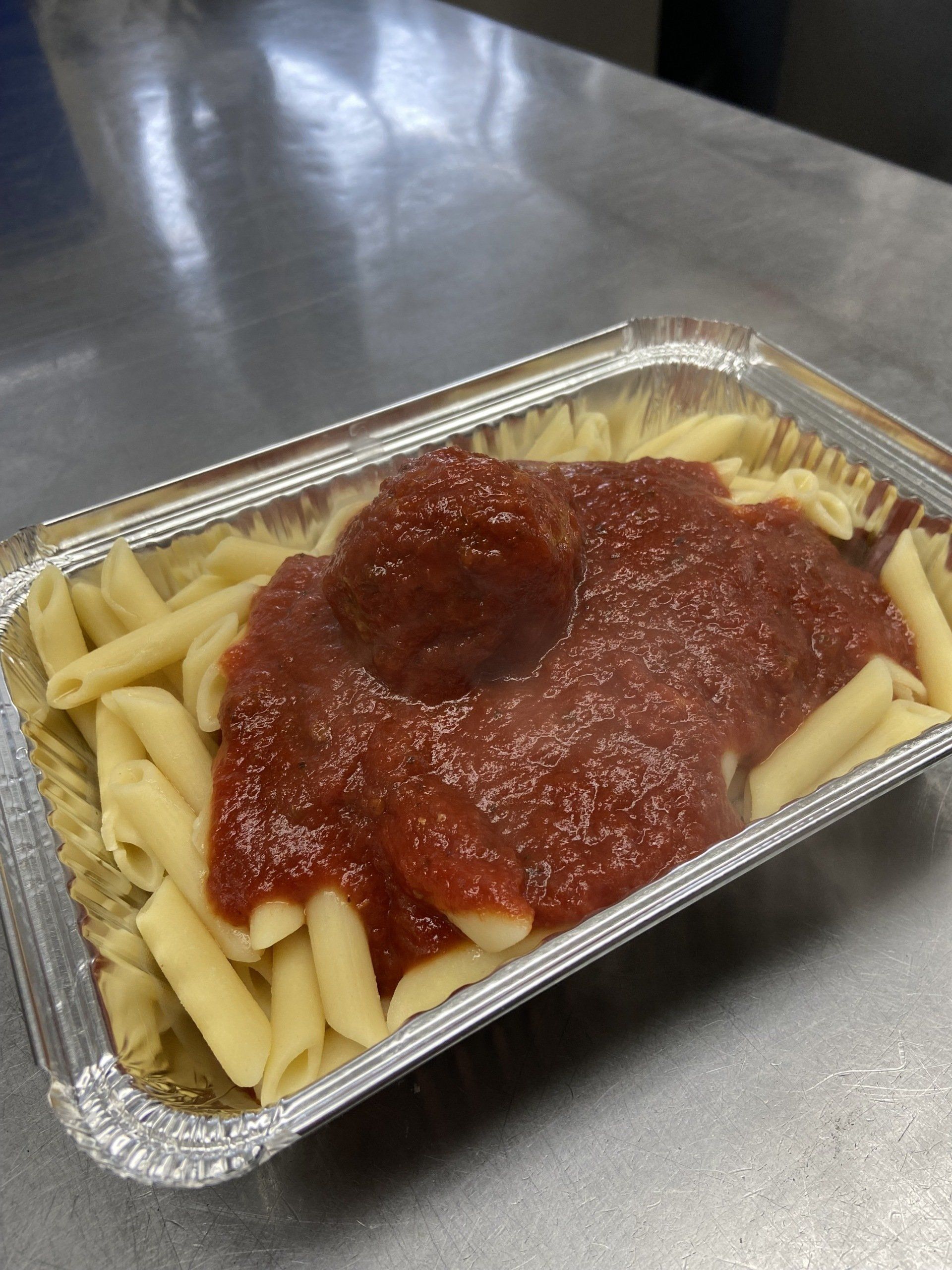 Penne pasta with red sauce and a meatball in a silver foil container.