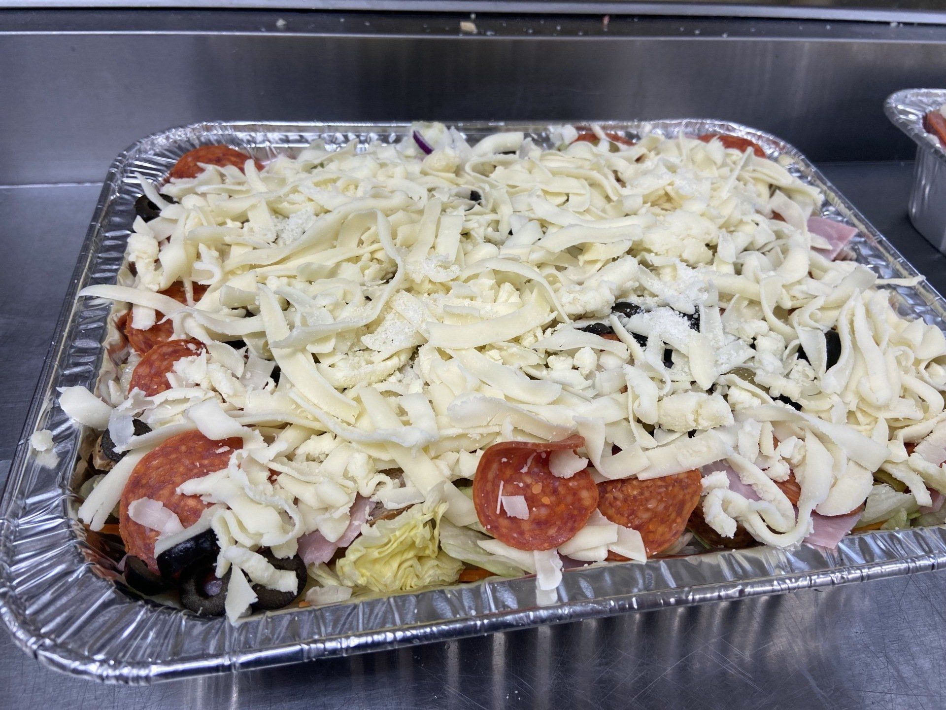 Pizza ingredients in a foil pan, topped with shredded cheese, ready to bake.