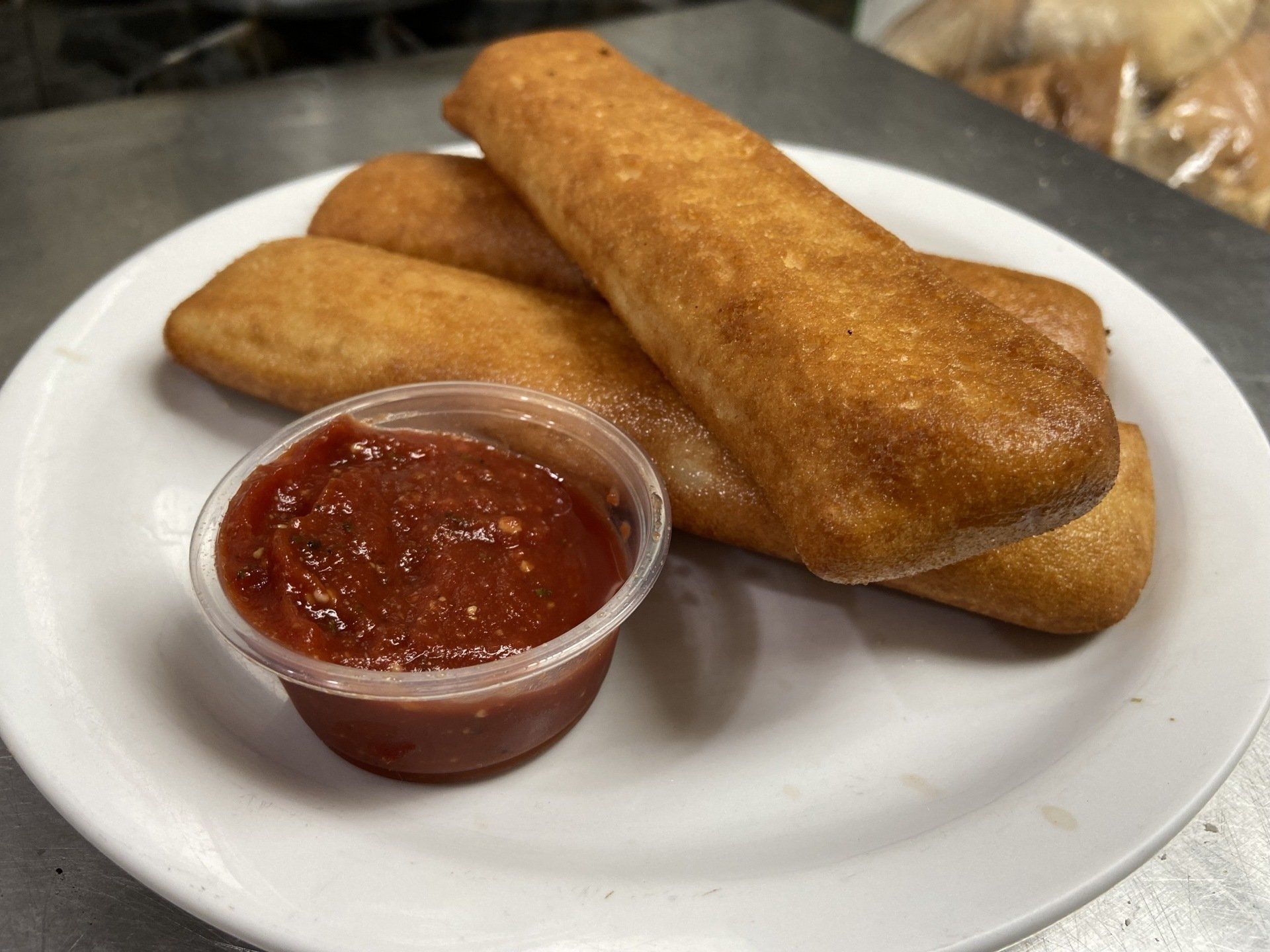 Fried dough sticks with marinara sauce in a small cup on a white plate.
