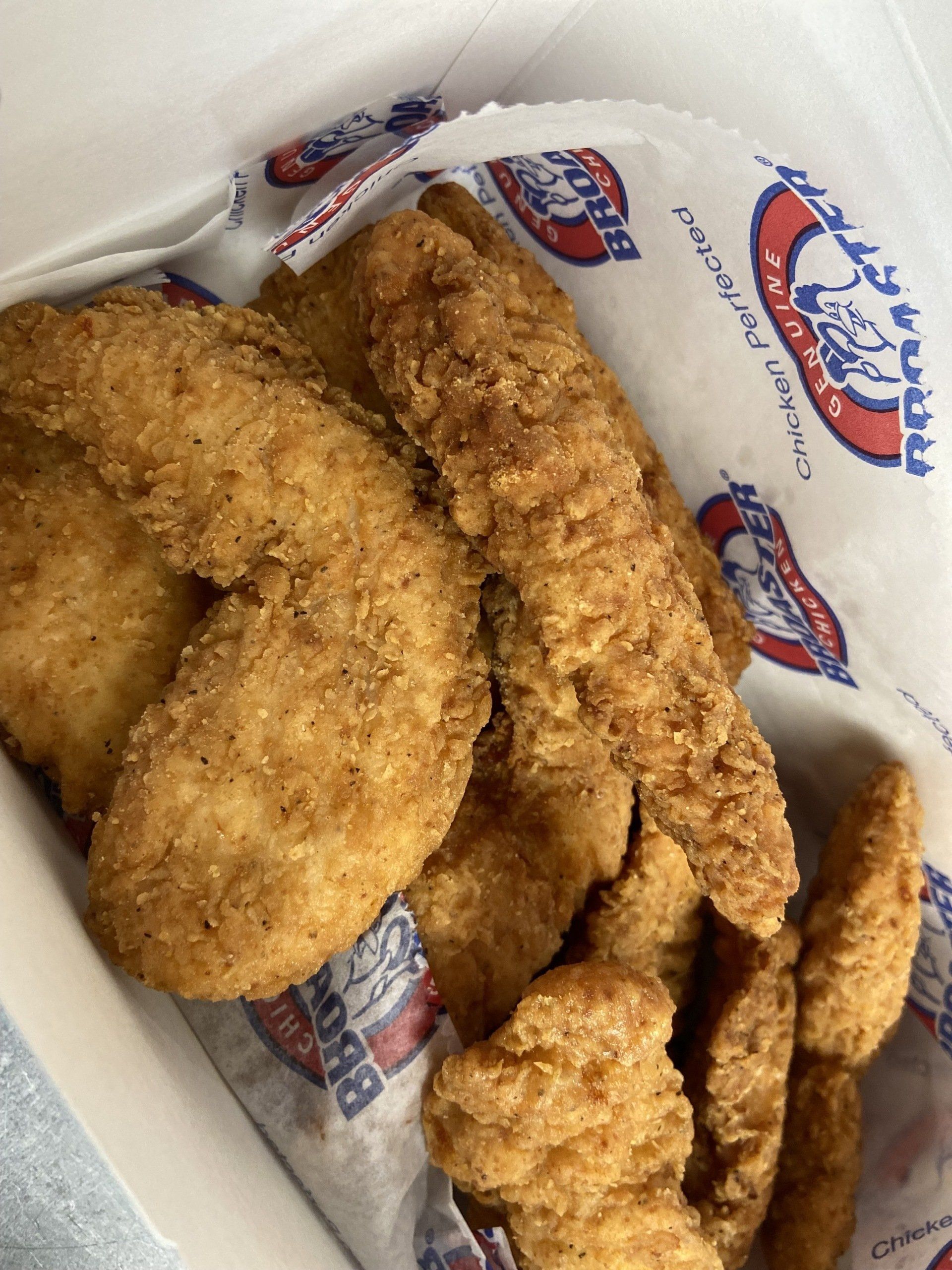 Crispy fried chicken tenders in a white box lined with branded paper.