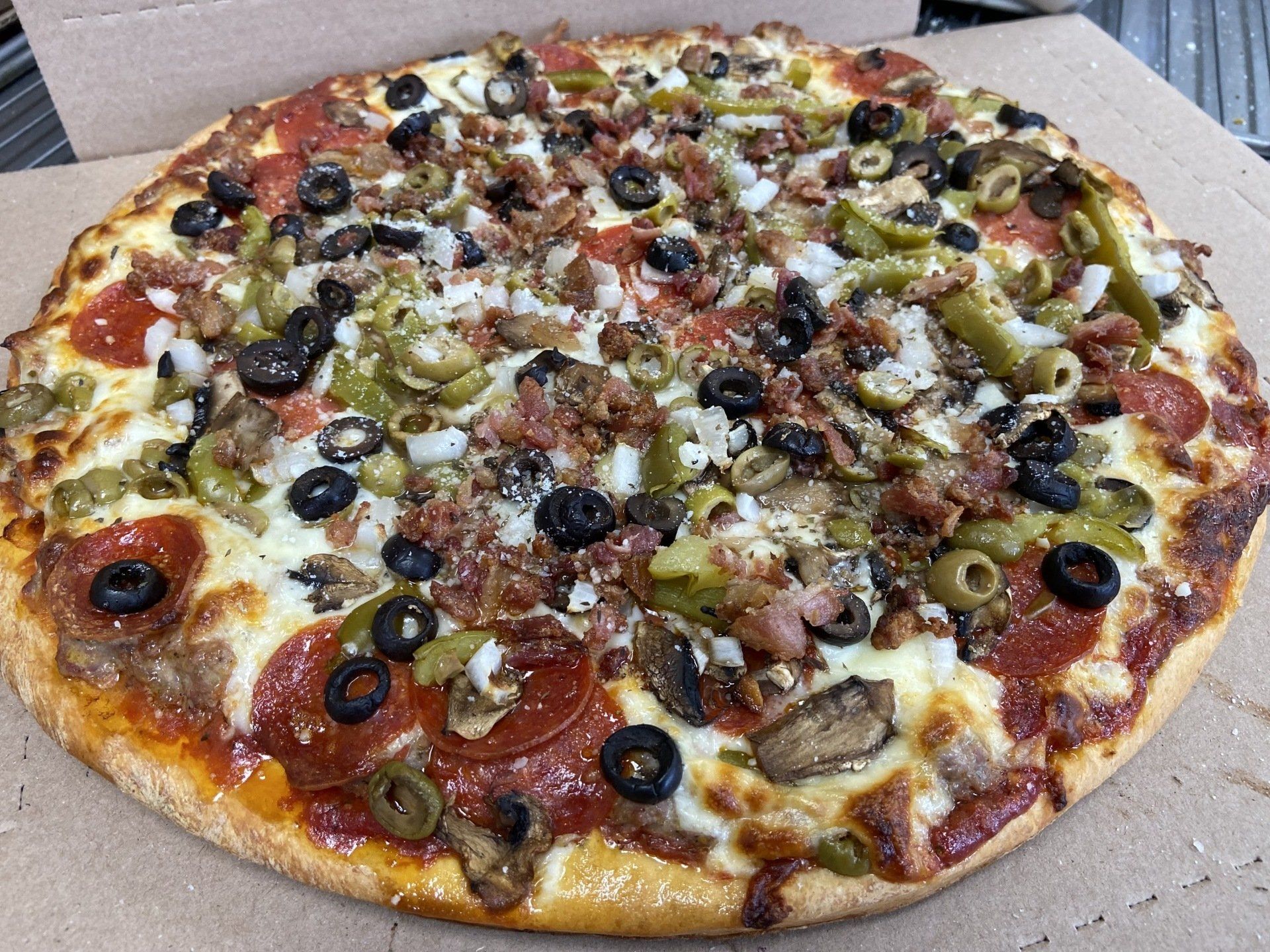 Pizza with pepperoni, olives, green peppers, mushrooms, and meat toppings.
