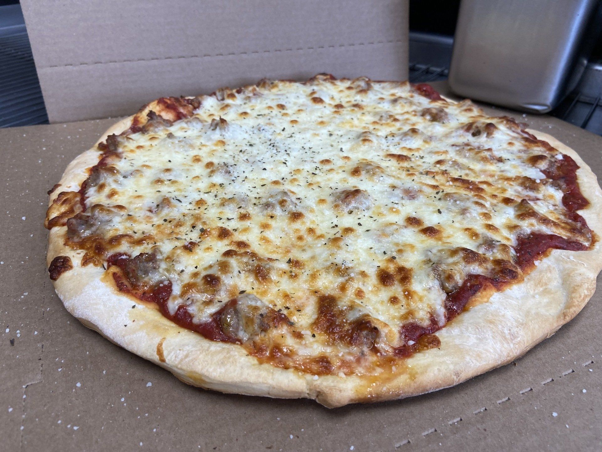 Pizza with sausage and melted cheese on a cardboard box.