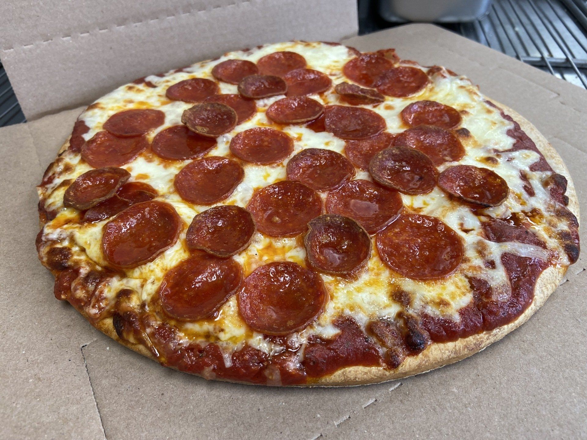 Pepperoni pizza in a cardboard box, topped with cheese and red pepperoni slices.