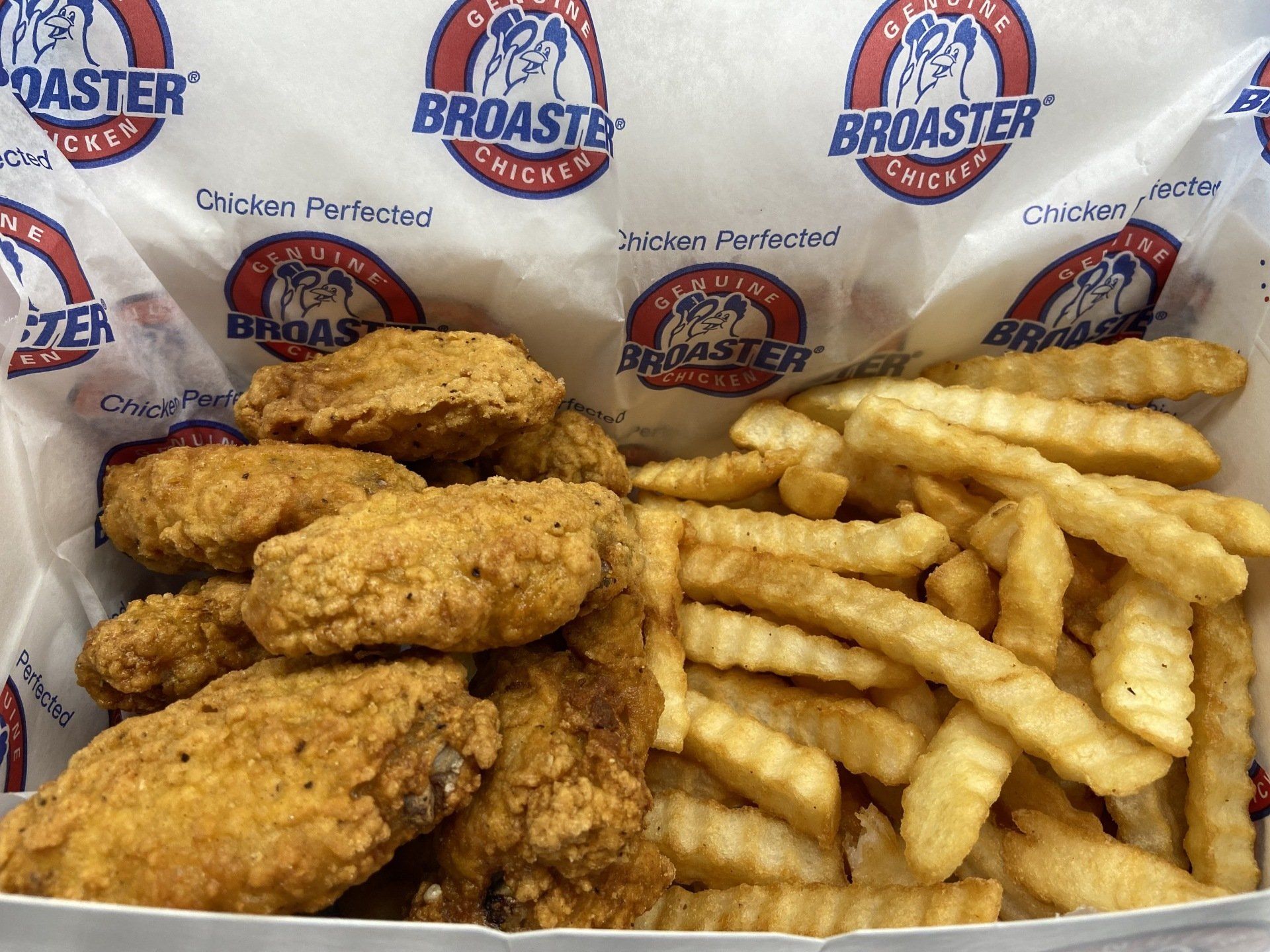Broaster chicken wings and crinkle-cut fries in a paper-lined basket, logo visible.