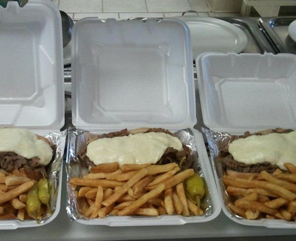 Three takeout containers with cheesesteaks, fries, and peppers.