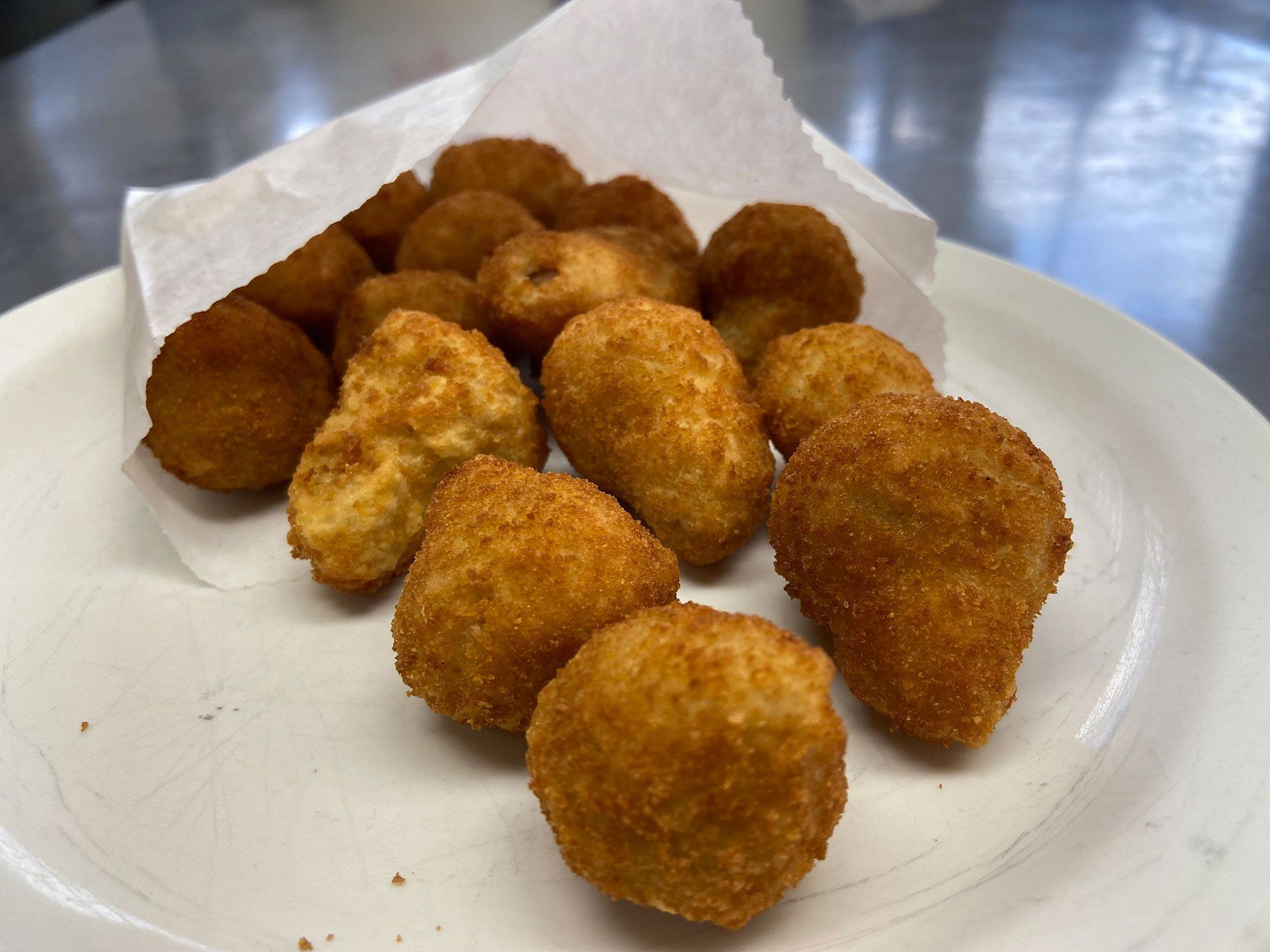 Golden-brown fried croquettes spilling out of a paper bag onto a white plate.