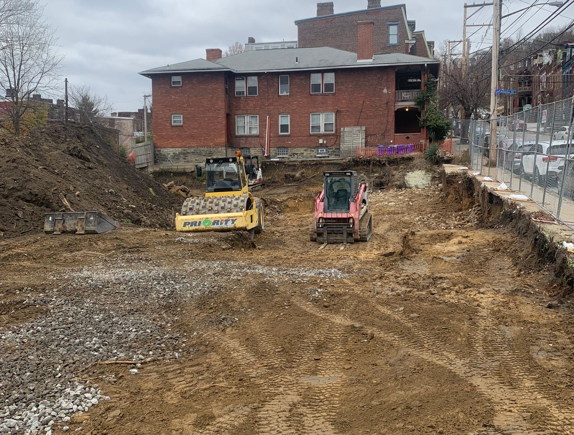 Construction site with heavy machinery excavating soil near a brick building.