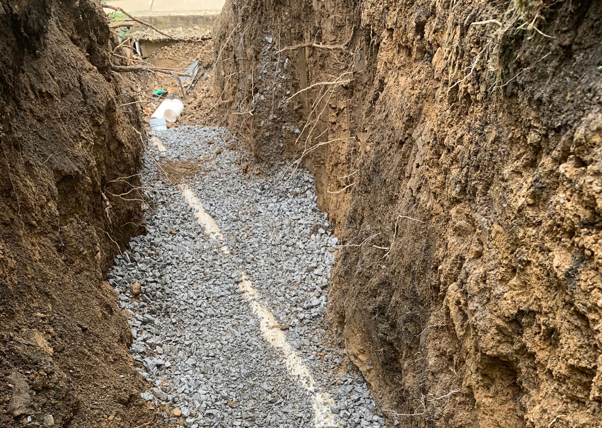 Trench filled with gravel, a white pipe running through it, and exposed dirt sides.