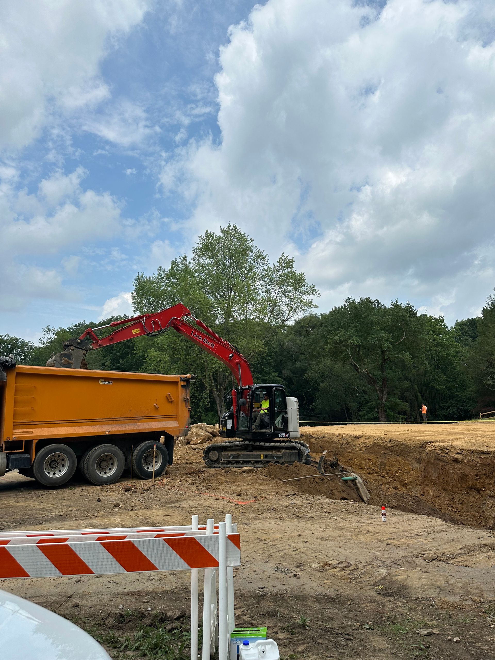 Excavator loading dirt into a dump truck at a construction site on a sunny day.