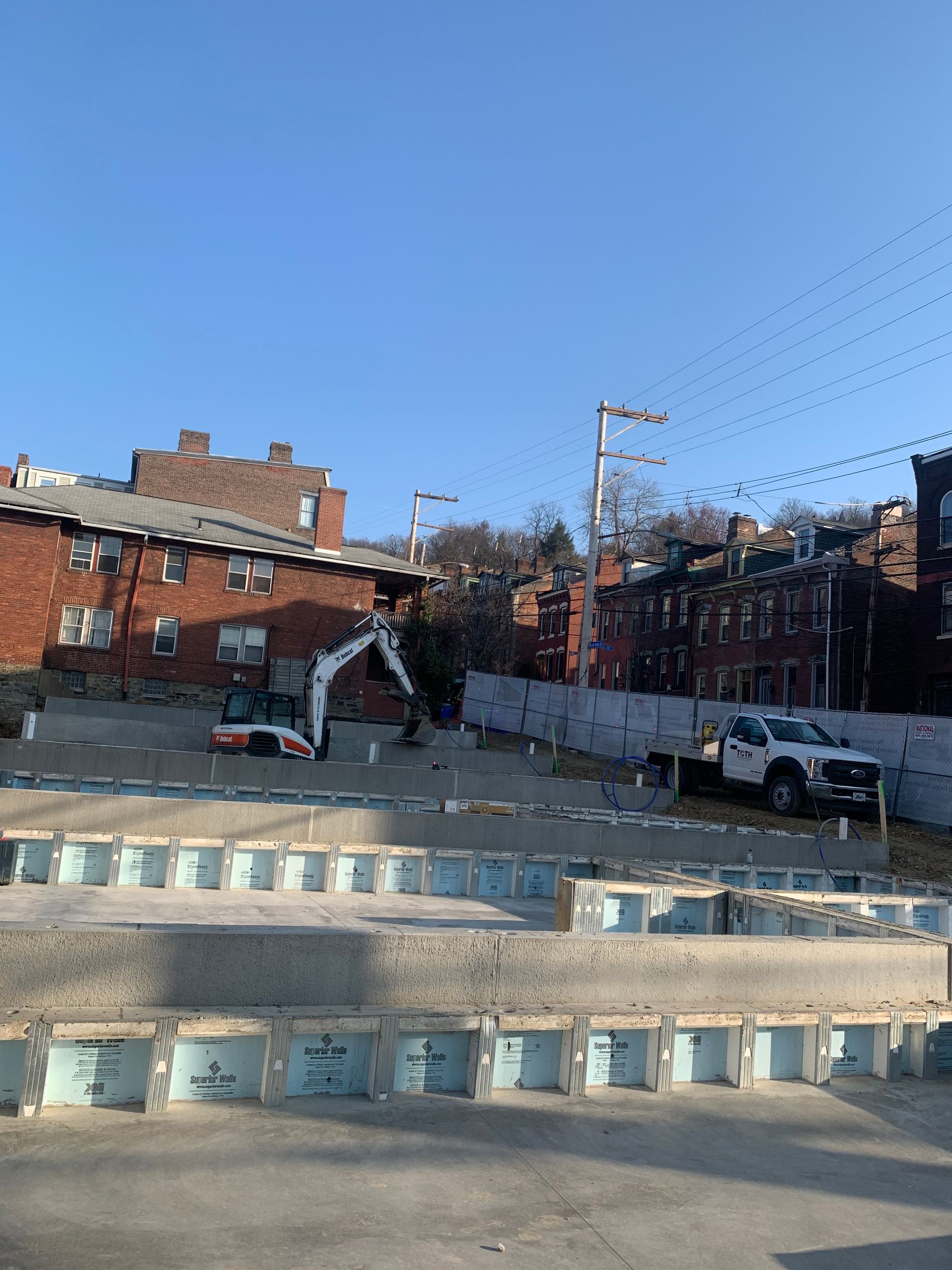 Construction site with excavator and truck. Buildings in background. Blue sky overhead.