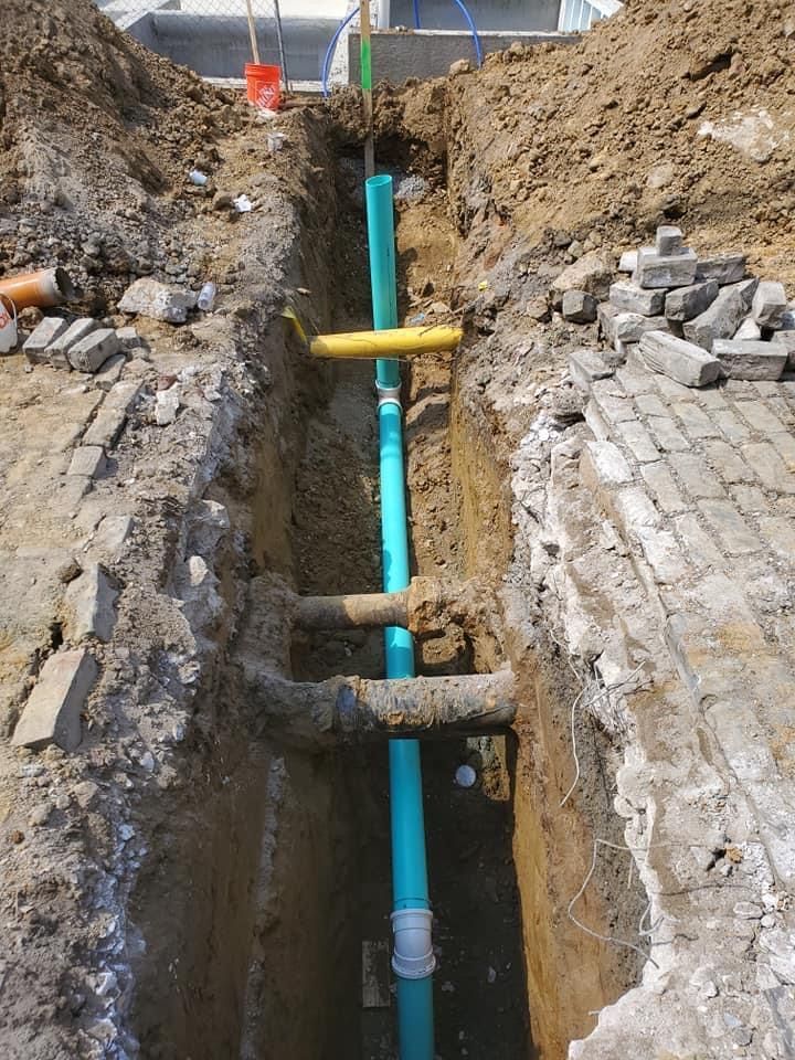 A trench with blue water pipes, yellow conduit, and old brickwork.