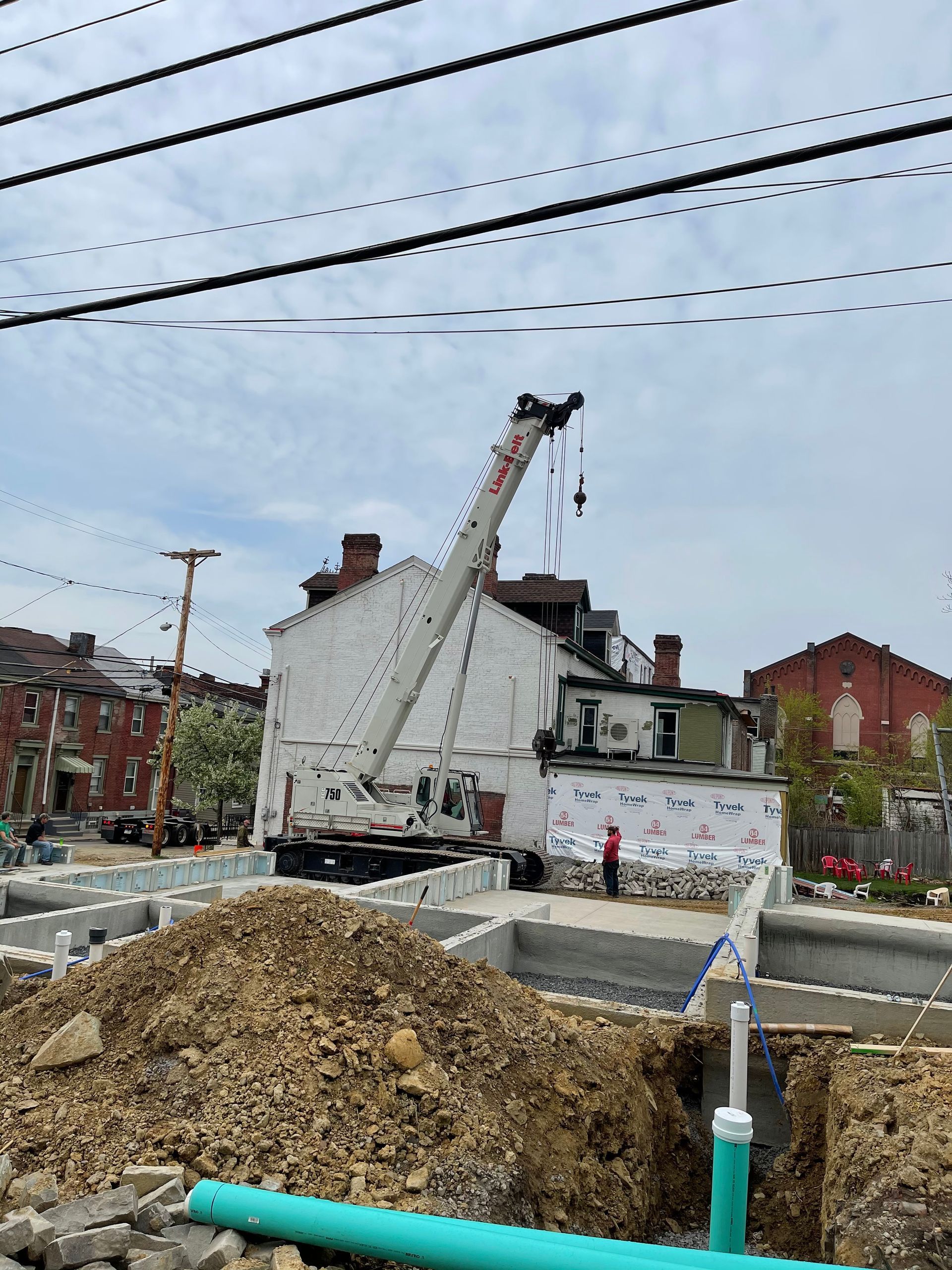 Construction site: Crane next to a building; foundation work in progress; cloudy sky.