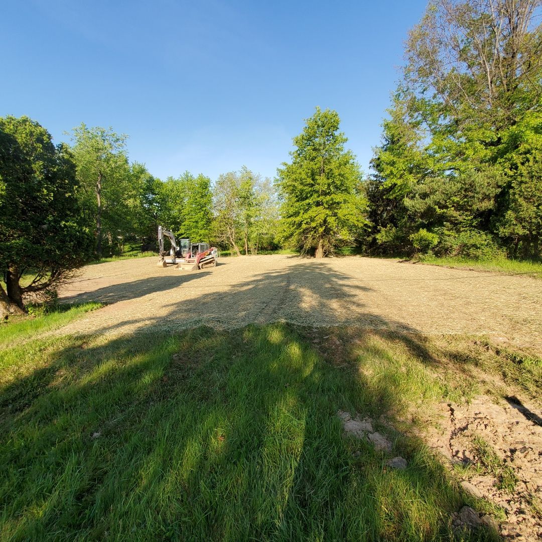 Clearing a field for construction, with excavators in the distance and trees surrounding.