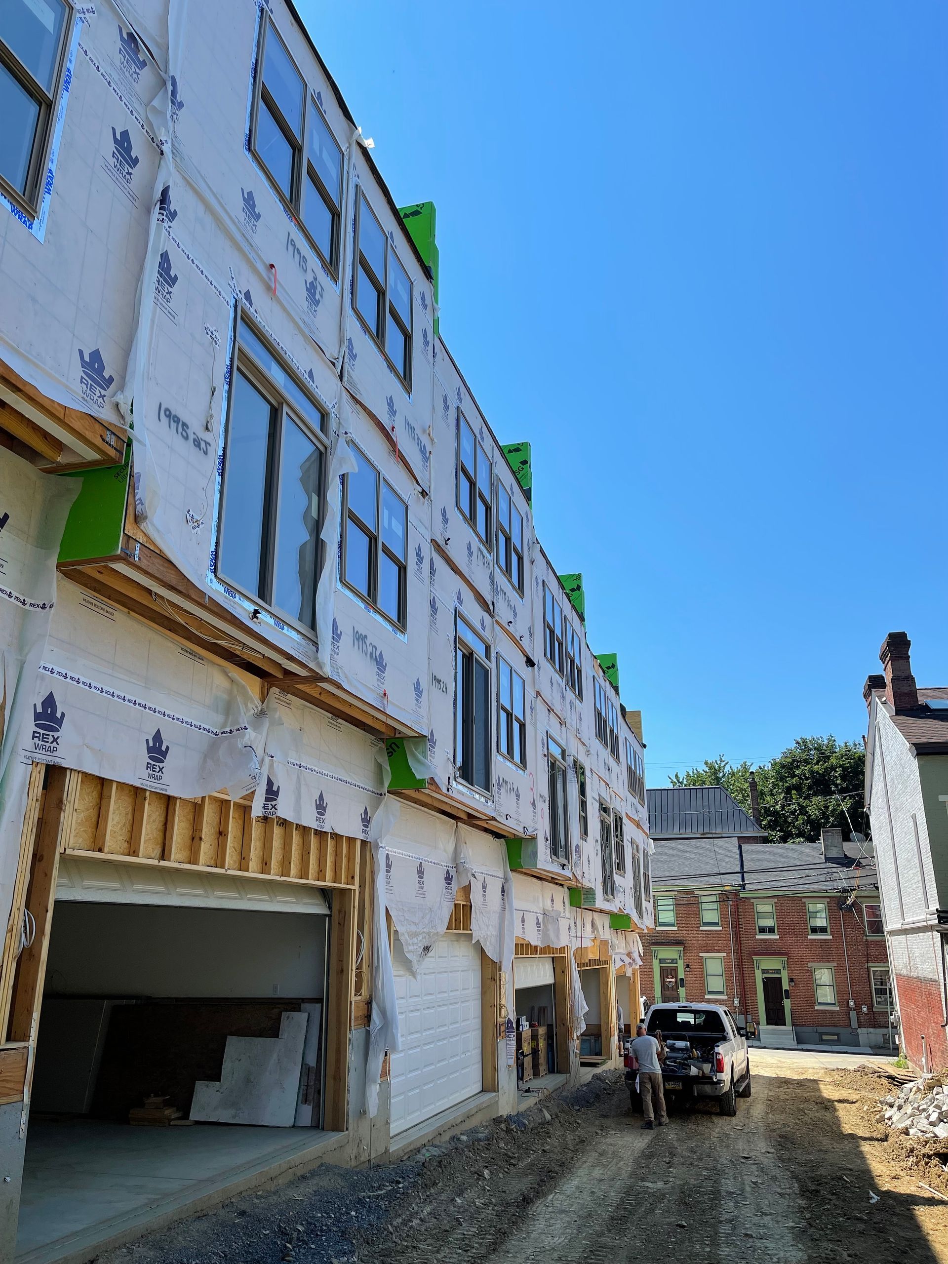 Multi-story building under construction with garage and nearby older buildings on a sunny day.