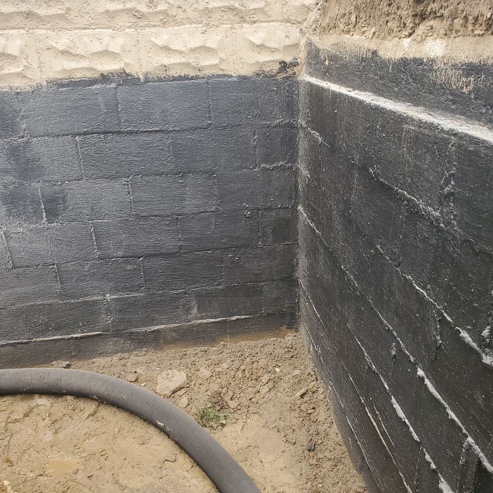 Foundation wall corner with black waterproofing membrane, in excavated setting.