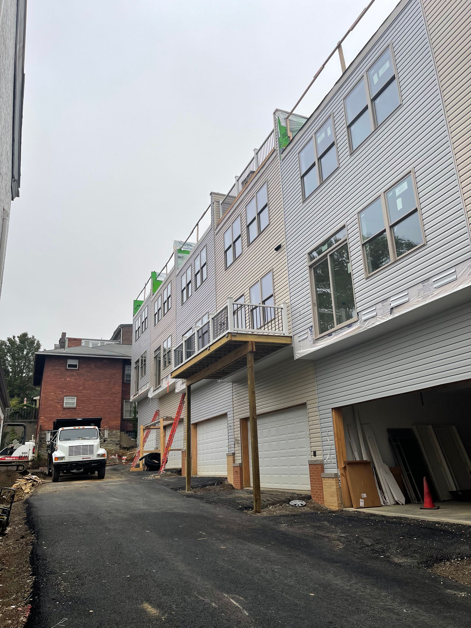 New construction townhouses with patterned siding, garage doors, and a truck on a paved road.