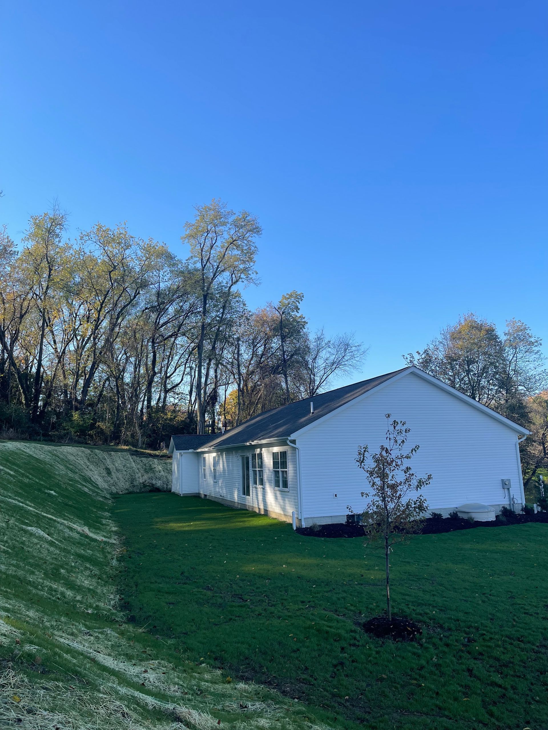 White house with a sloped roof and green lawn against a backdrop of trees under a bright blue sky.