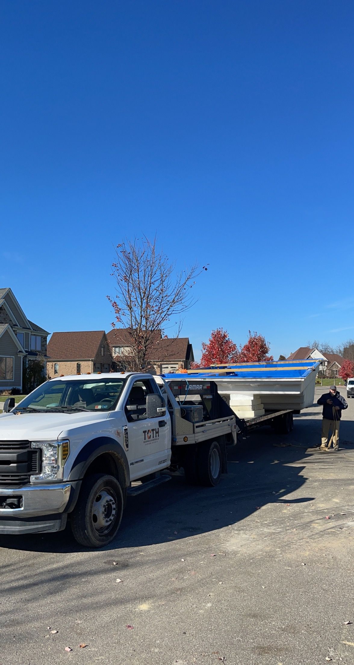 White truck towing a white trailer carrying a large blue and white structure on a sunny day.