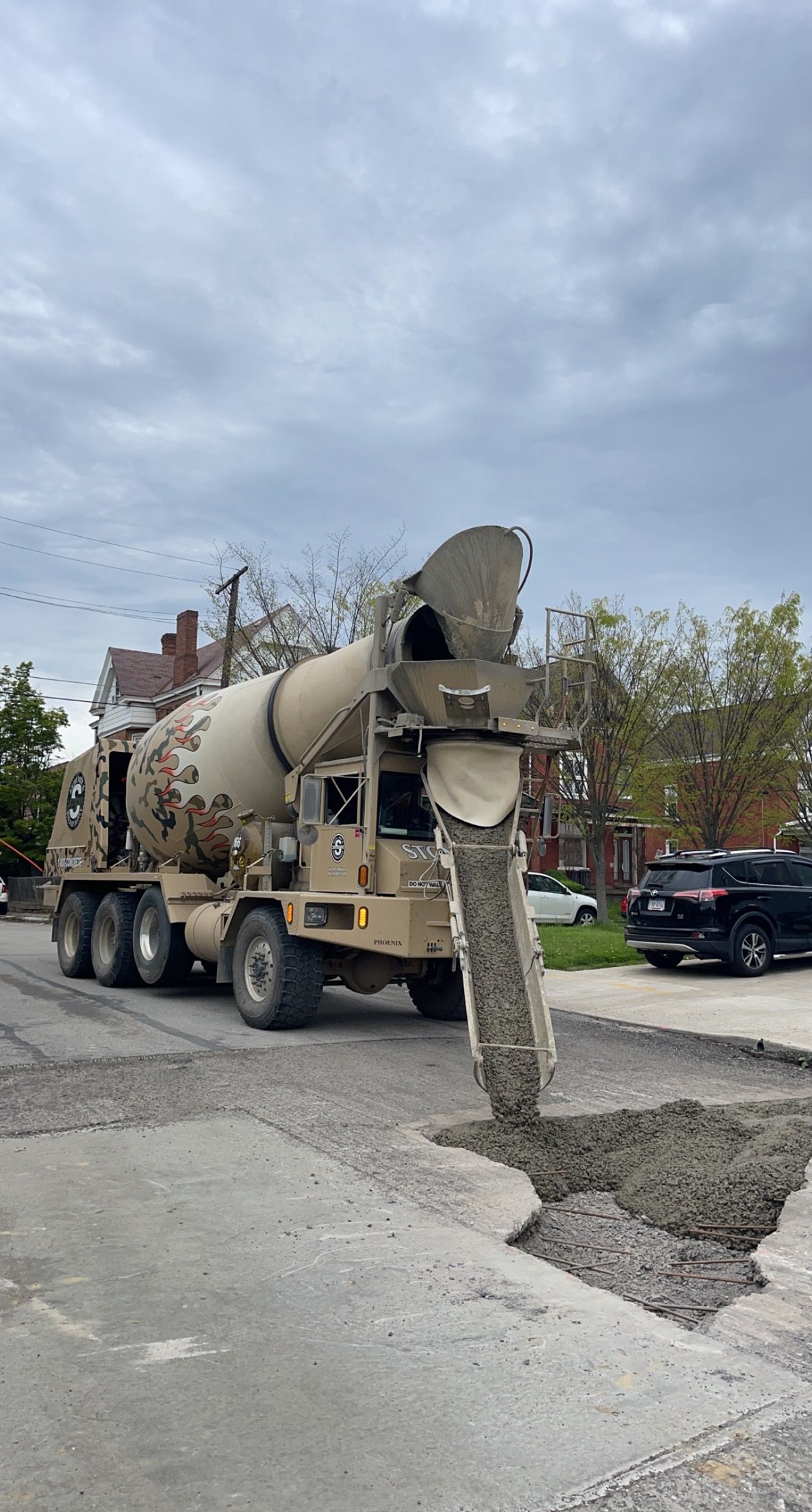 Concrete truck pouring wet concrete into a damaged street on a cloudy day.