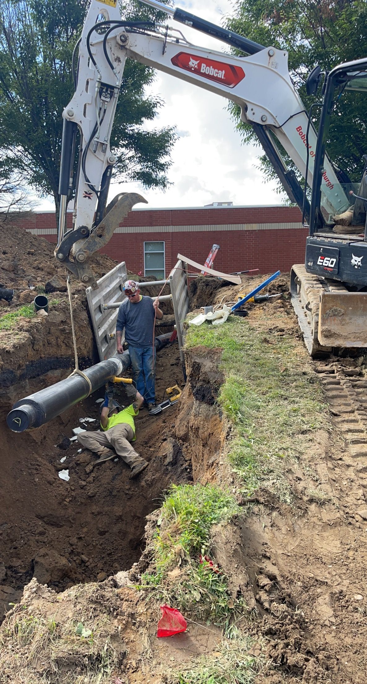 Construction workers installing a pipe in a trench, using an excavator.