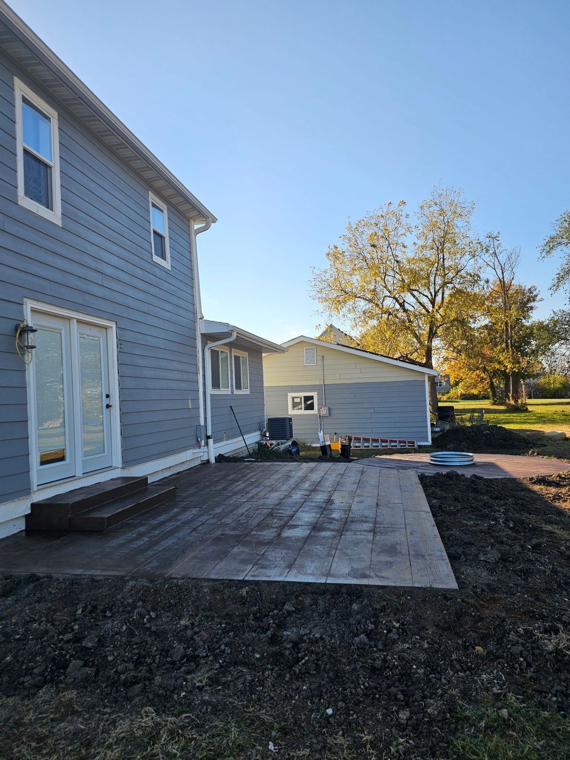 Backyard with a gray house and a recently installed patio of gray pavers.